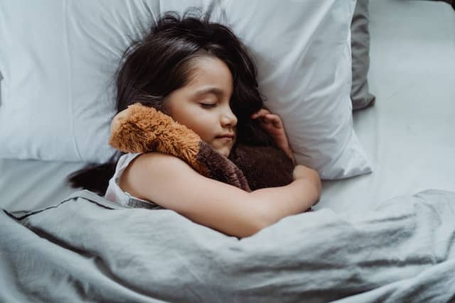 A girl sleeping tightly with her teddy because there are Himalayan salt lamps in her home.