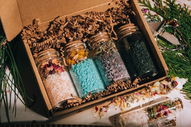 A box filled with four jars of dried herbs and bath salts portraying the health and beauty benefits of salt baths.