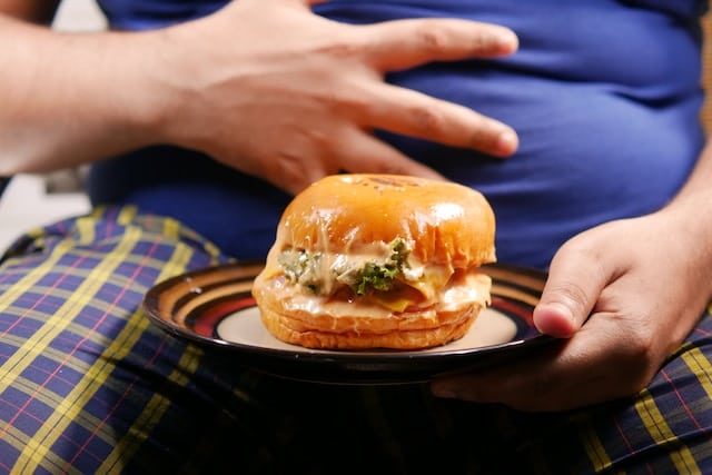 Person holding their belly in pain after eating a hamburger