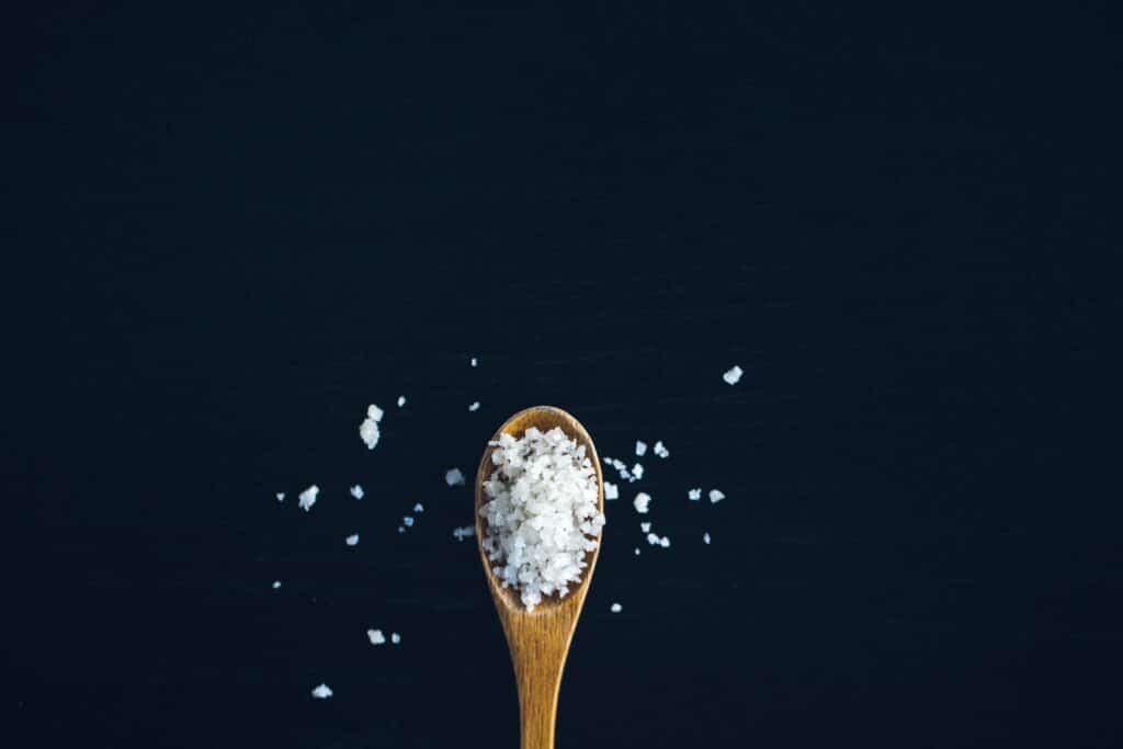 a wooden spoon with salt on a dark background