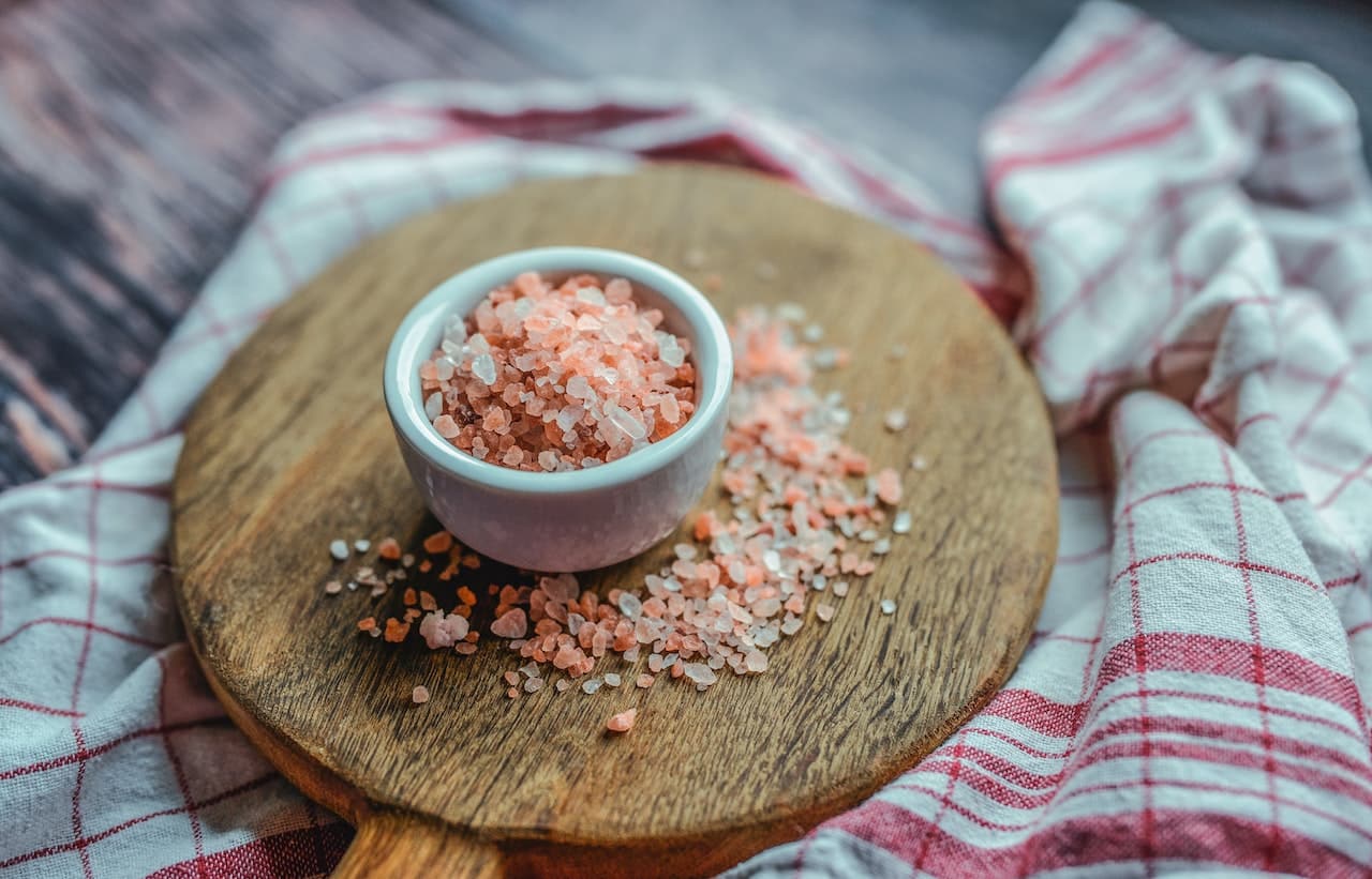 a bowl of pink and white salt on a wooden board