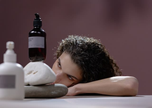A woman with curly hair lying near fragrances bottles.